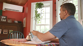 Man sitting at a table operating a heat pump with a remote control.