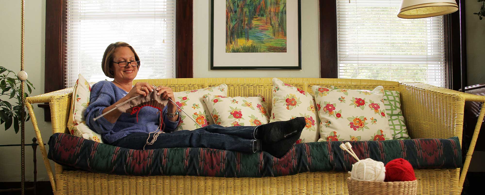 A woman sitting on a couch while she enjoyingly knits.