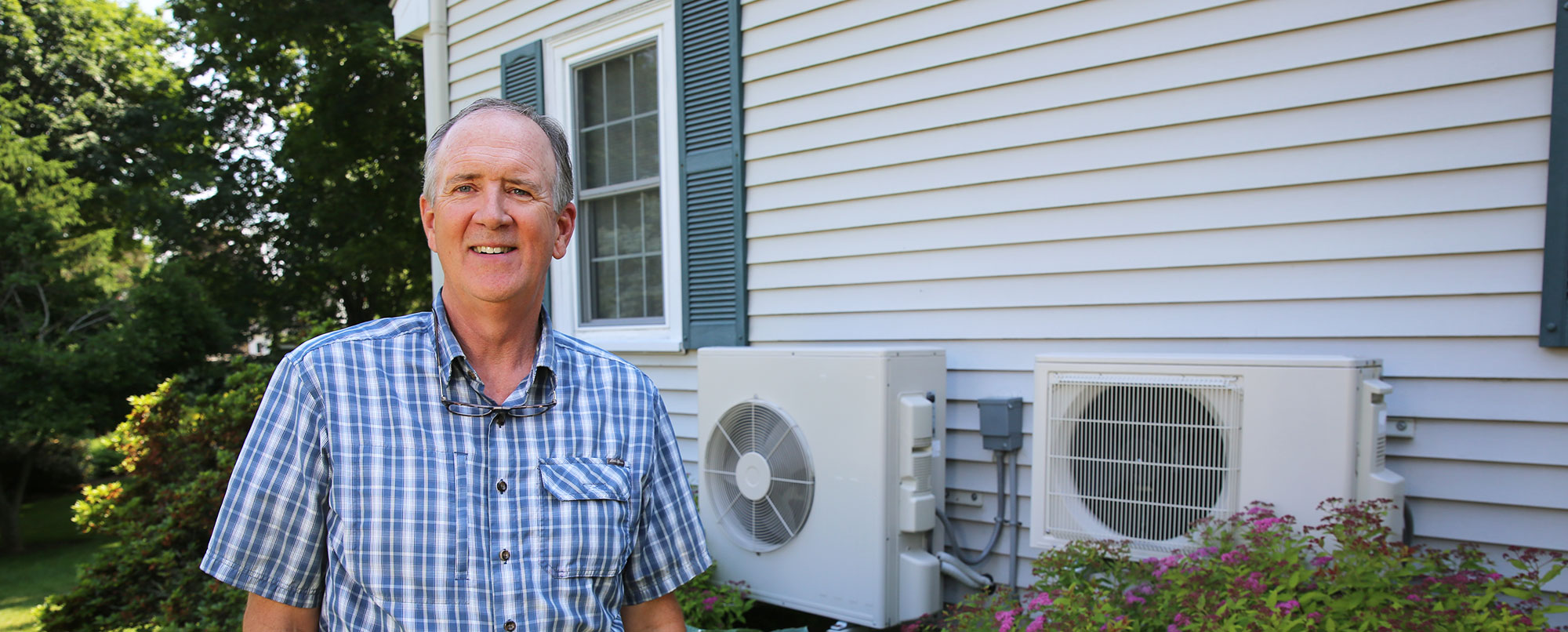 A happy homeowner standing near his heat pump outdoor units.