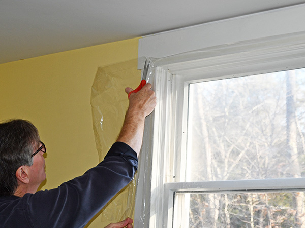 A man insulating his window with a clear cover.